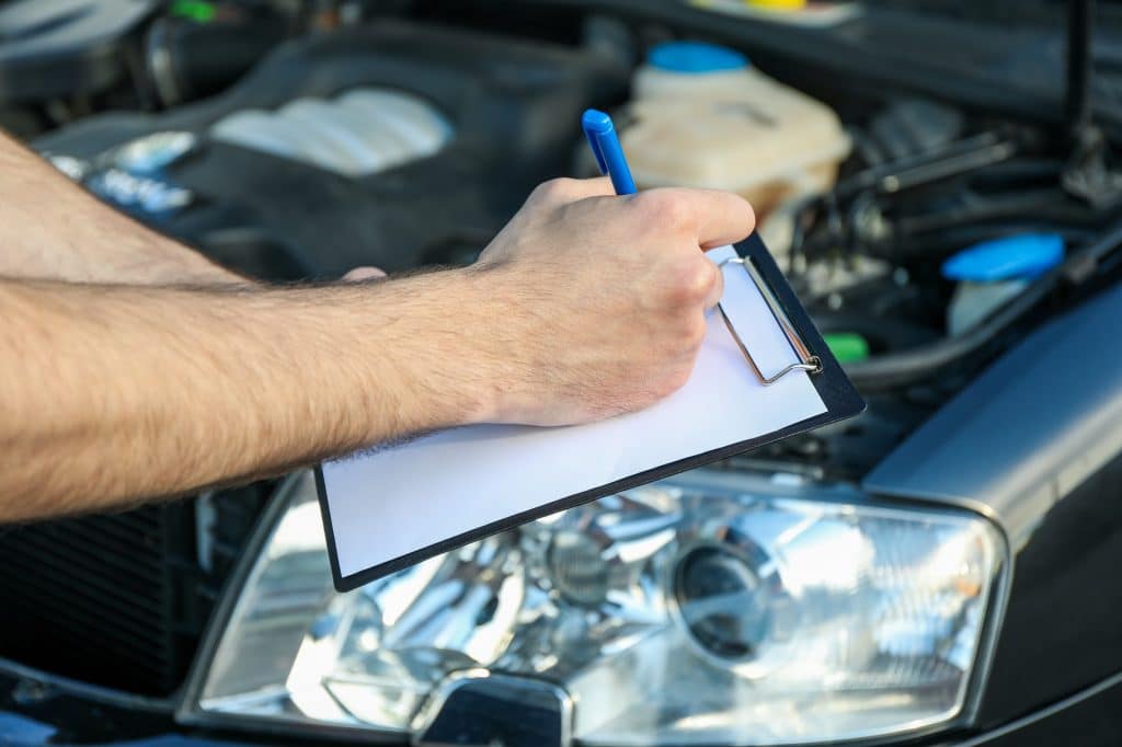 A man in overalls writes to a clipboard. Mechanic. Car inspection